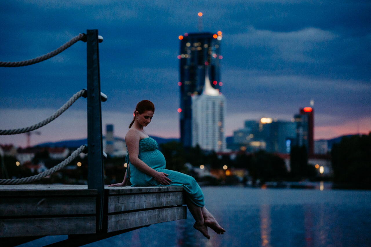 Stolze Schwangere bei Daemmerung in der Skyline von Wien an der alten Donau fotografiert beim Babybauchshooting von Fotograf Markus Winkelbauer